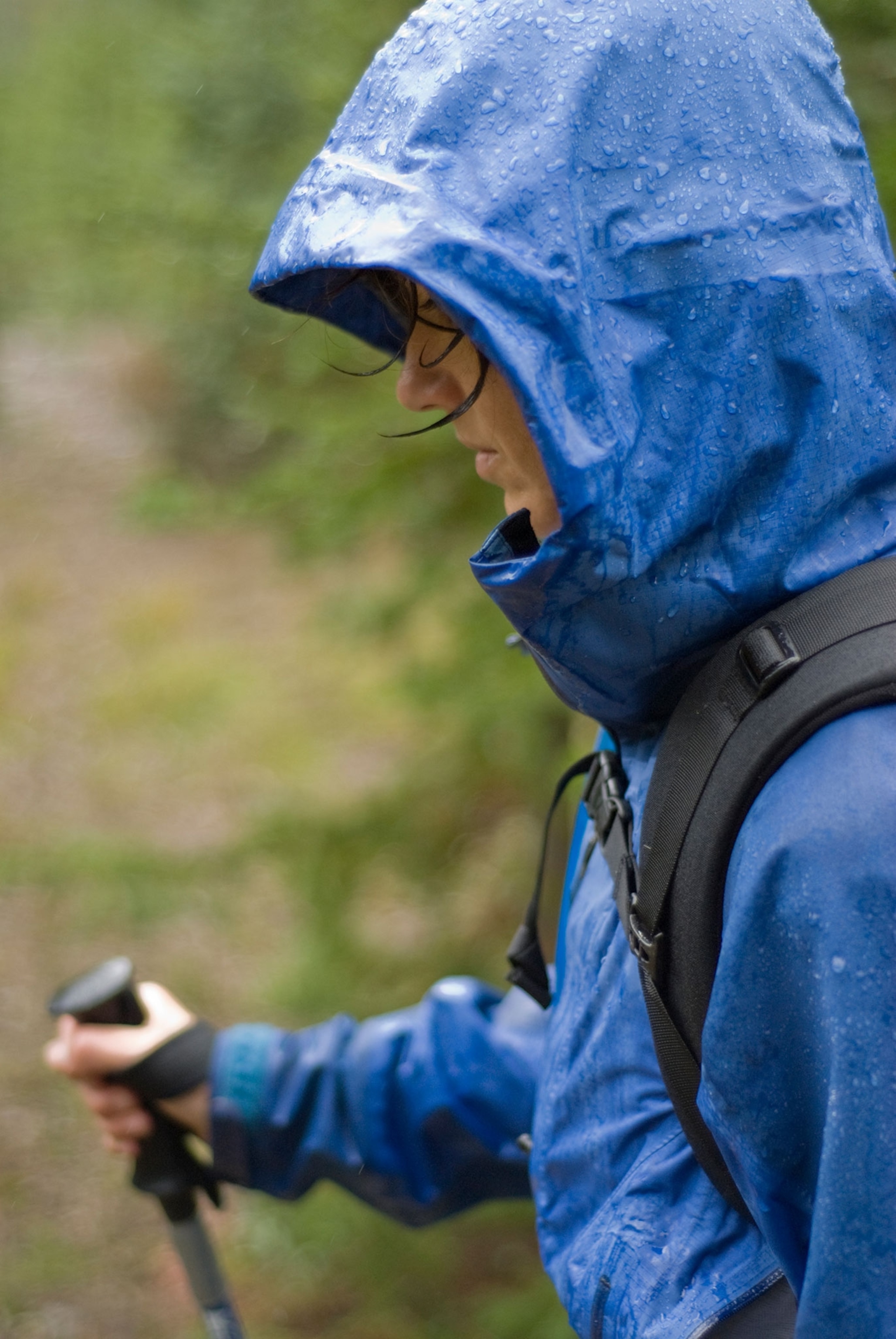 Woman hiking in a blue rain jacket with walking stick and backpack in the rain.