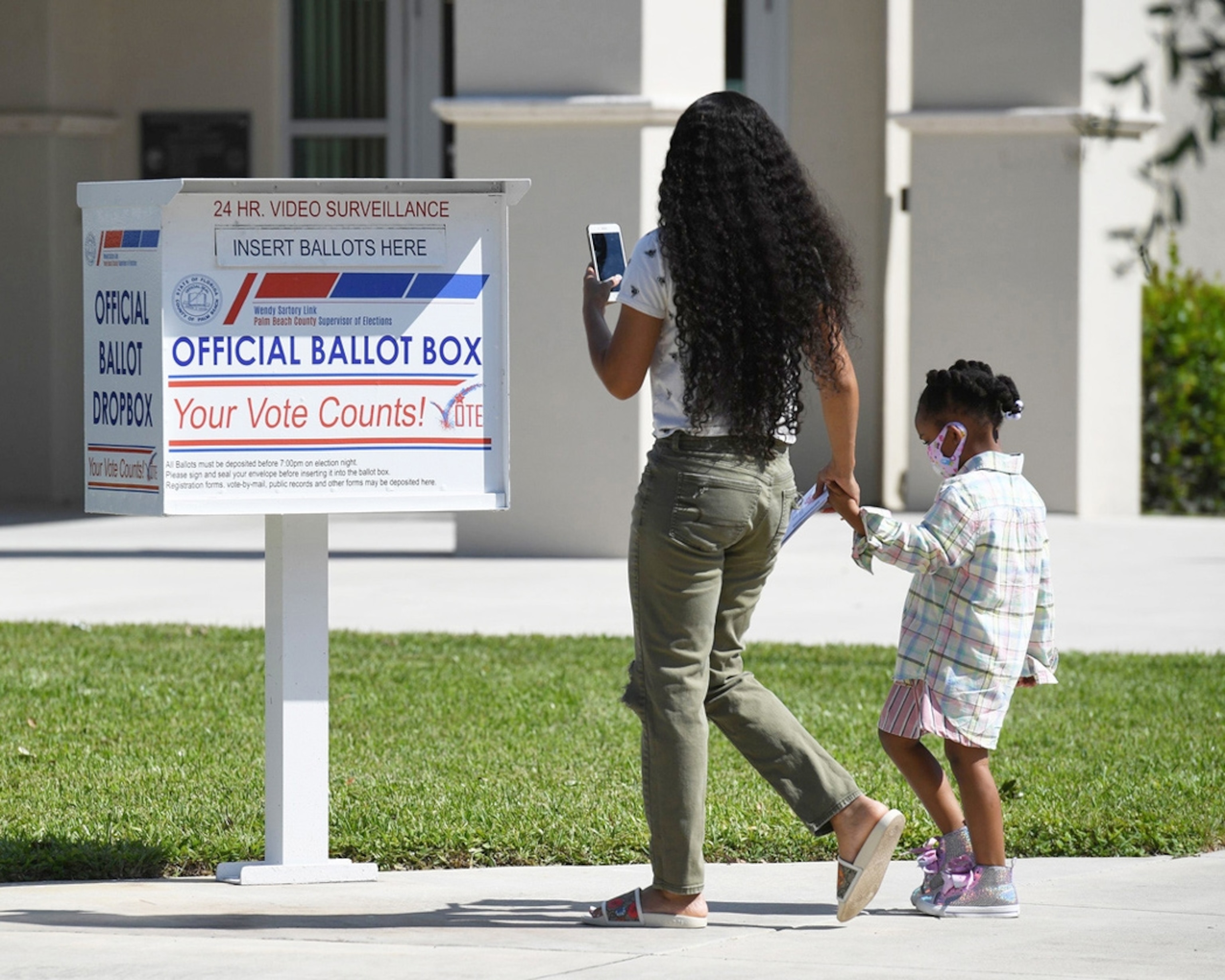 A Woman with her child drops off her vote by mail ballot.