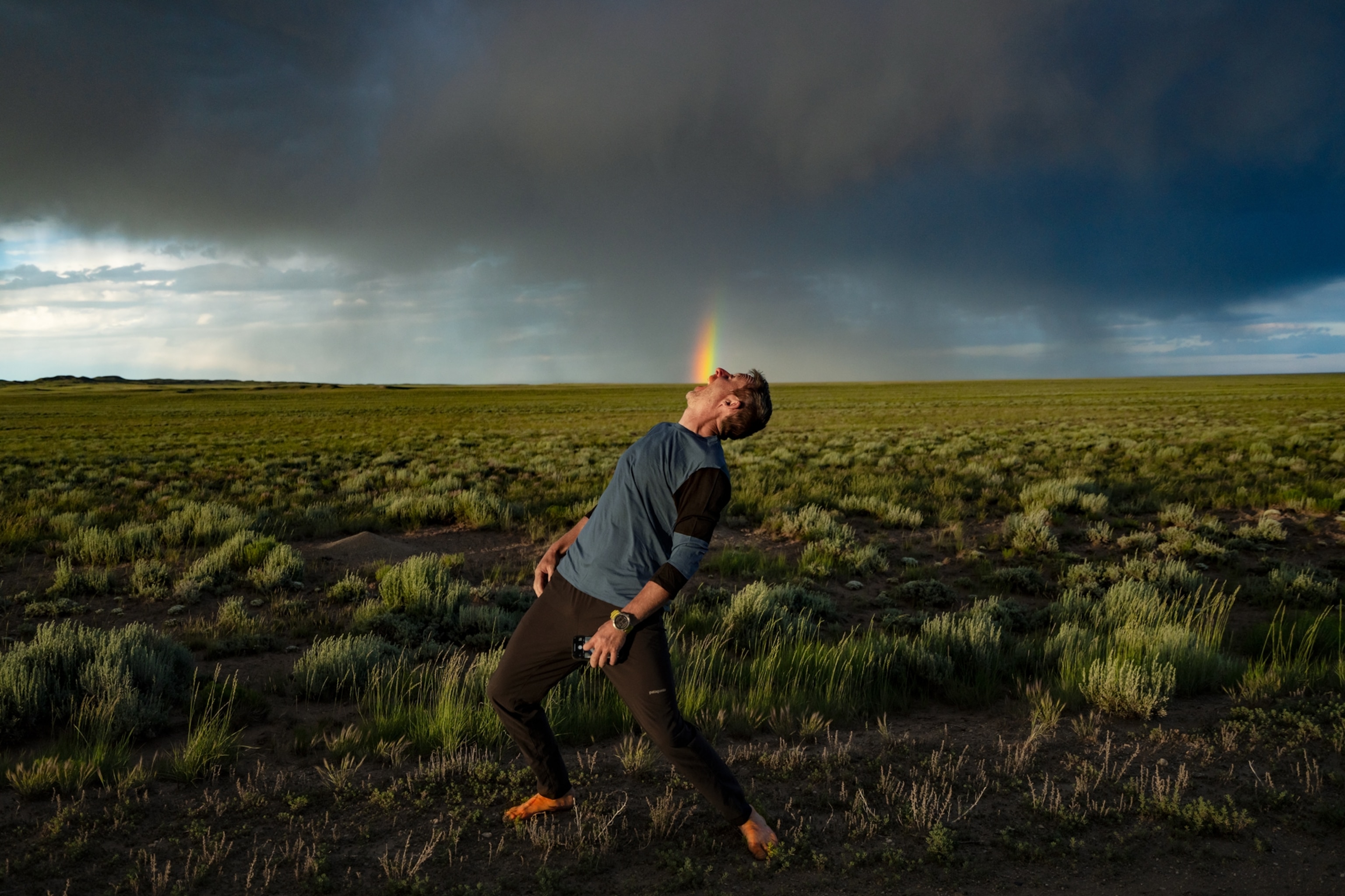 a man standing in front of a rainbow leaning to the side with his mouth open- giving the illusion of eating the rainbow