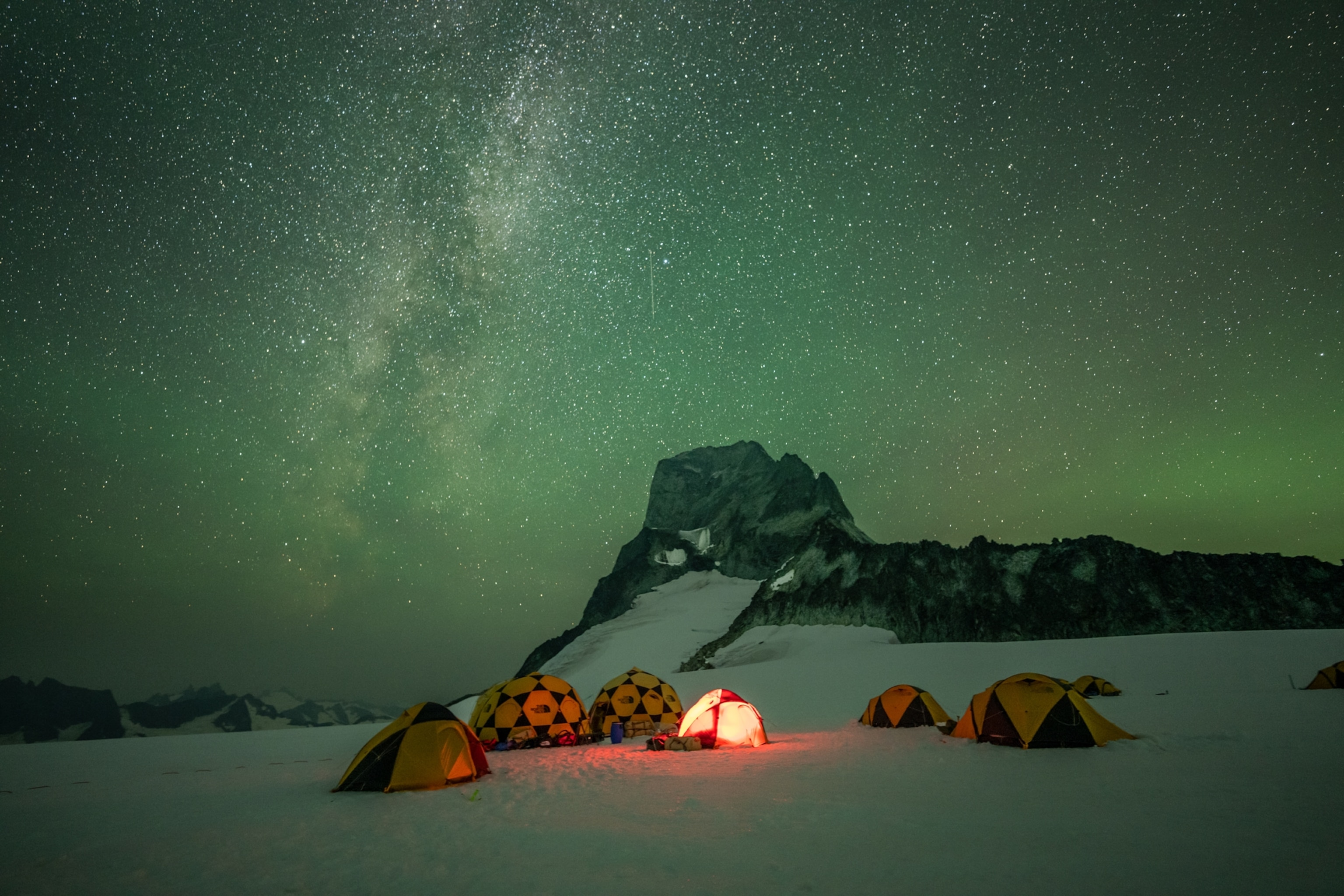 tents in the snow at night below the green starry sky