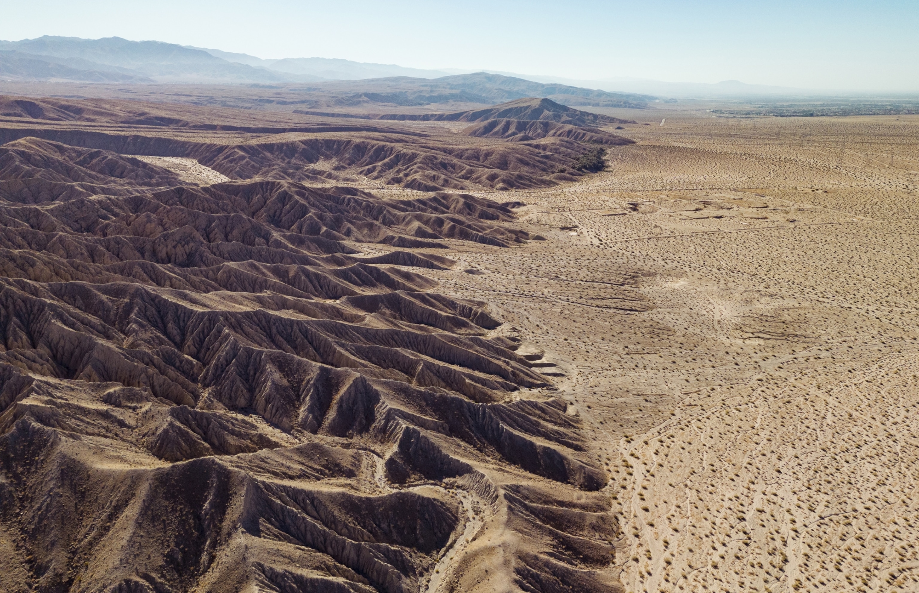 A birds eye view of the San Andreas Fault. The left half of the image looks very rugged, with sharp pointed mountains. The right side shows the flat desert land.