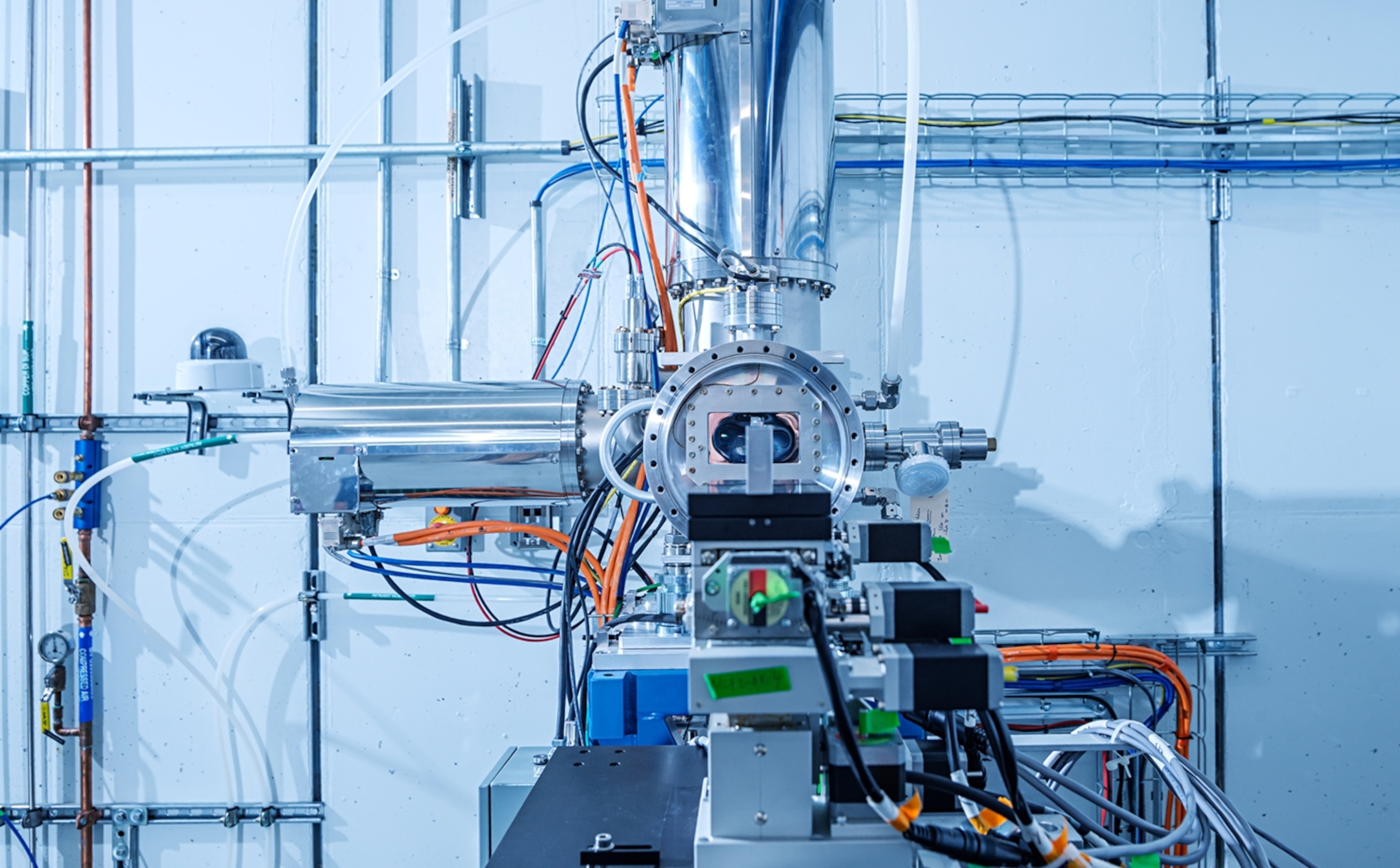 A silver piece of equipment sits in a laboratory. There are orange and black wires coming out of it.